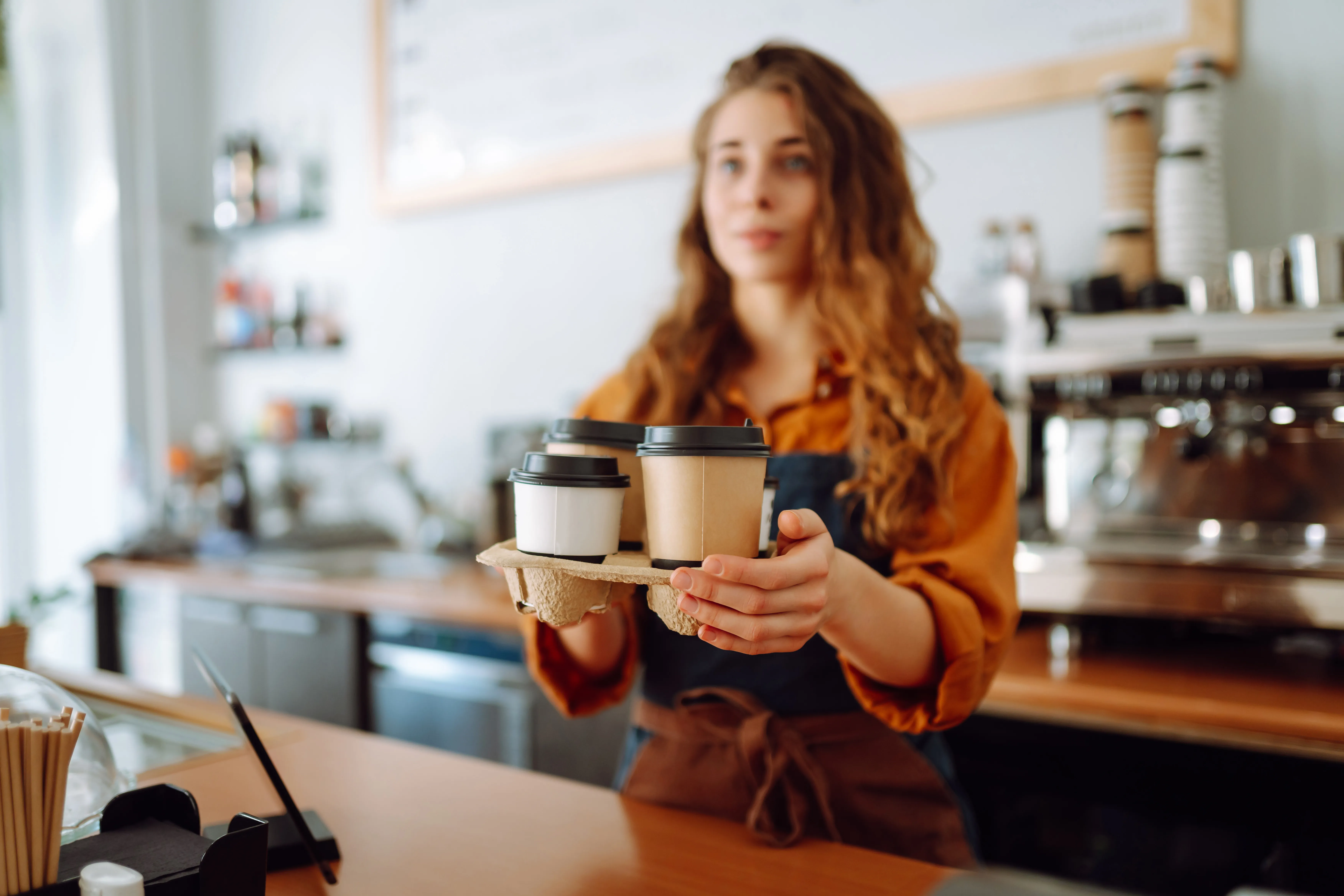 A roaster holding out two takeaway cups on a tray across the counter